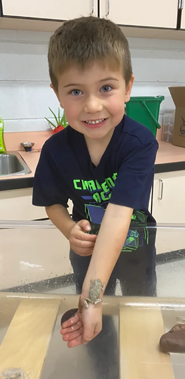 A student shows off a frog sitting on his forearm.