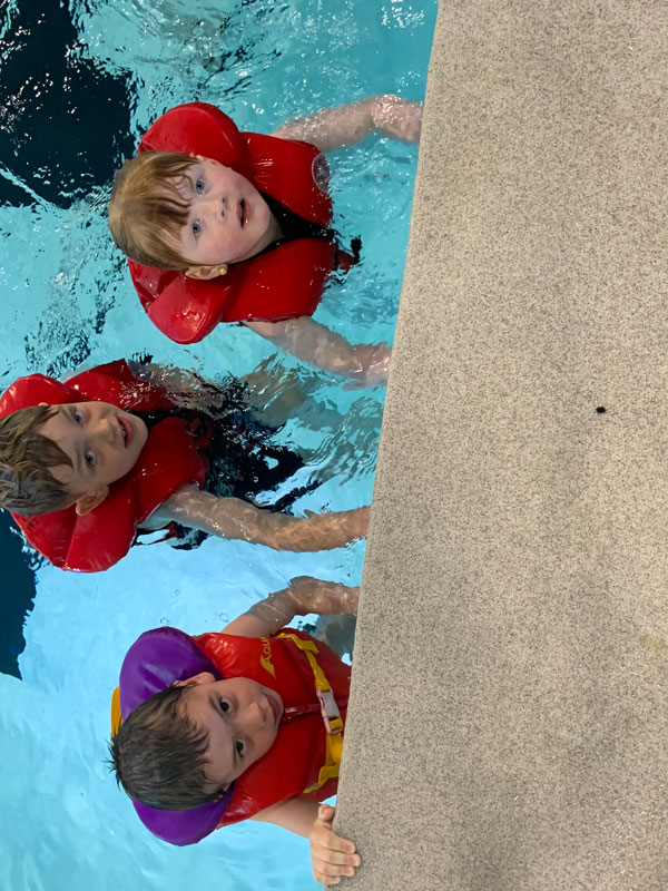 Three kids wearing lifejackets in a pool