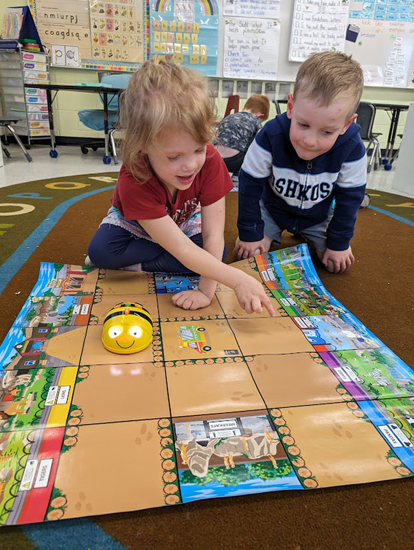 Two boys look at a large coding graphic on the floor