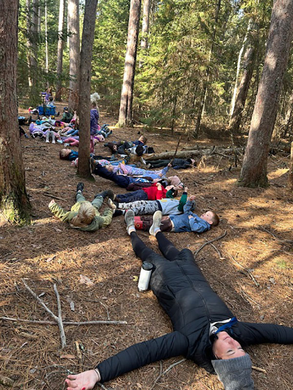 Students and staff lay on the forest floor looking up at the trees and sky