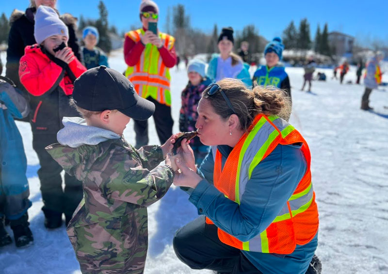 Volunteer kissing a fish that a student is holding for her at a winter fishing event