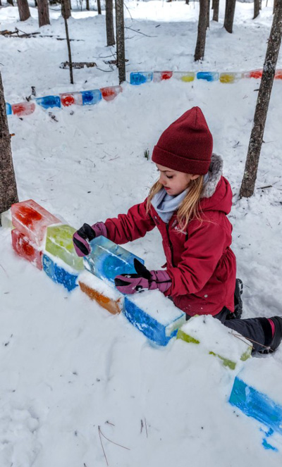 A girl helps build a wall from coloured ice blocks at Festival du Voyageur