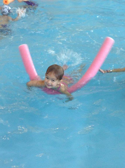 A boy swims with the aid of a pool noodle at the local swimming pool